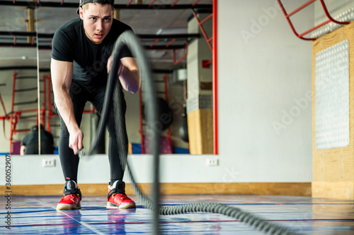 Portrait shot of strong young man training with battle ropes in the exercise gym