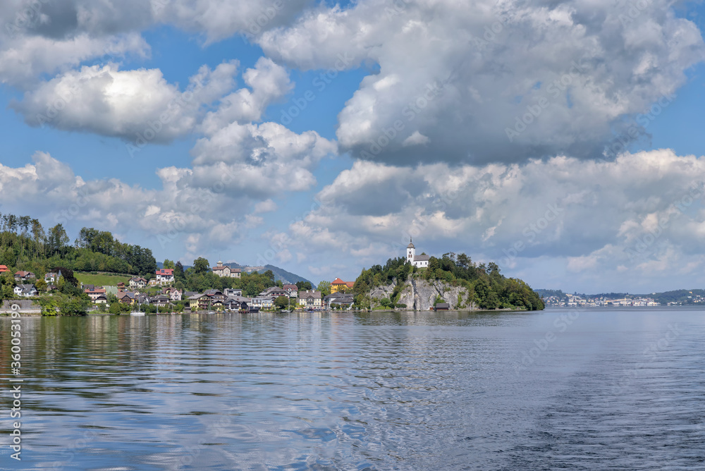 Fototapeta premium View over Lake Traunsee to the village Traunkirchen near Gmunden with Johannesberg Chapel under scenic clouds in the sky. Salzkammergut, Upper Austria, Europe
