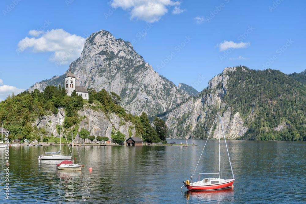 Scenic view of Lake Traunsee at Traunkirchen with sailboats and the Johannesberg Chapel on a rock, alpine mountains in the background. Salzkammergut, Upper Austria, Europe
