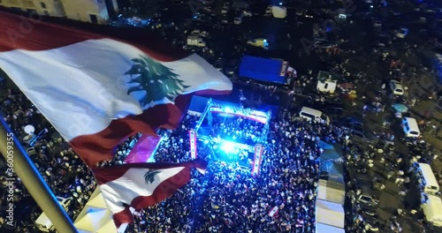 Beirut, Lebanon 2019: night turn around drone shot in martyrs' square, passing by Lebanese flag in foreground with protesters around a stage revolting against government during the Lebanese revolution photo