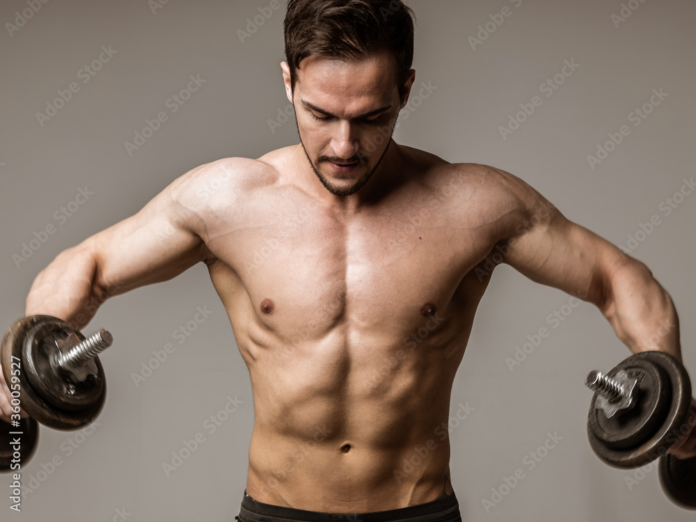 portrait of a muscular athlete with dumbbells on a light white background