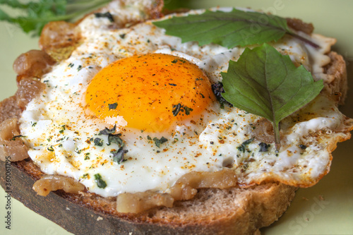 fried eggs with bacon and spices and basil leaves on a slice of brown bread