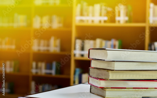 Stack of books on wood table and blurred bookshelf in the library, education background, back to school concept.