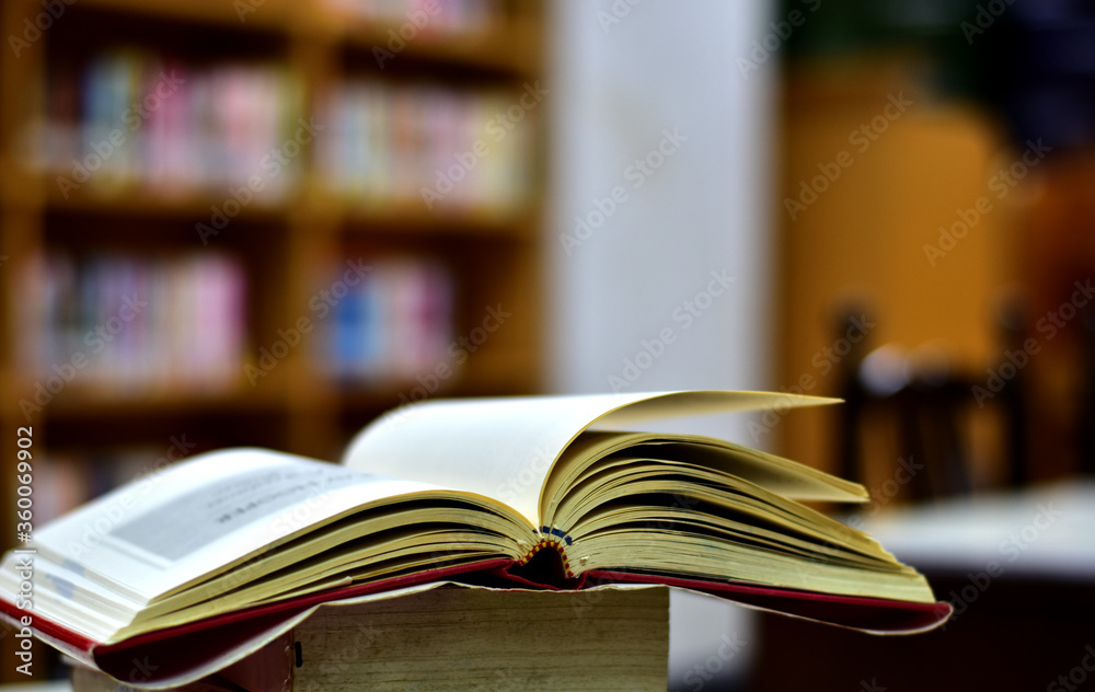 Fototapeta premium Open Book on wood table and blurred bookshelf in the library, education background, back to school concept.