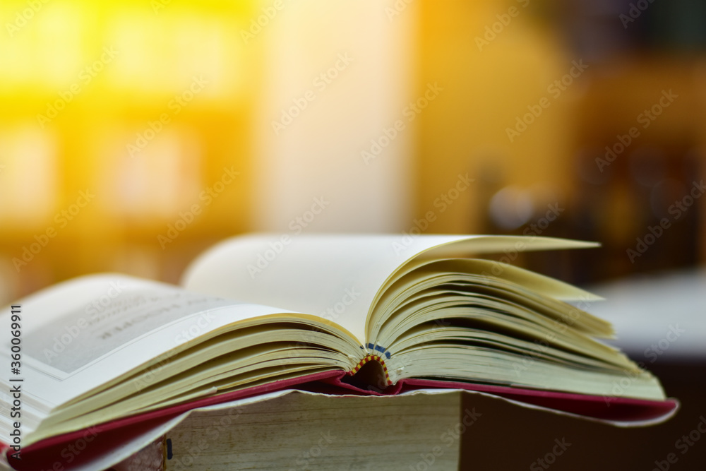 Naklejka premium Open Book on wood table and blurred bookshelf in the library, education background, back to school concept.
