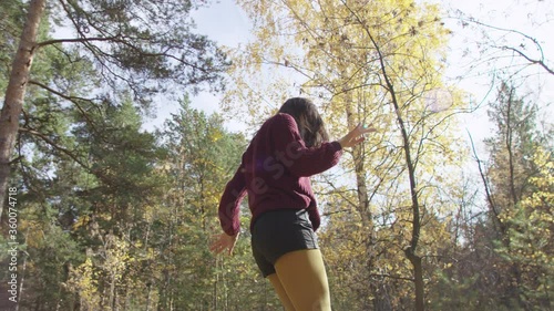 4K low angle portrait of female dressed in red jumper, black shorts and yellow tights dancing happily in the middle of autumn forest. 360 degree tracking arc shot.
