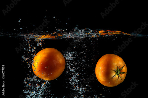 two tomatoes splash on water and black background 