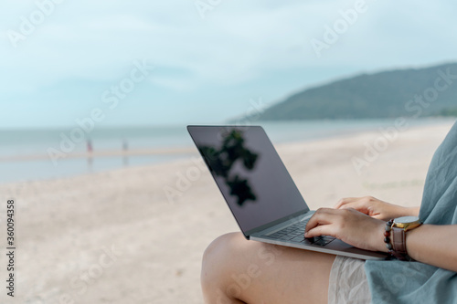 Woman using laptop and smartphone to work study in vacation cady at beach background.