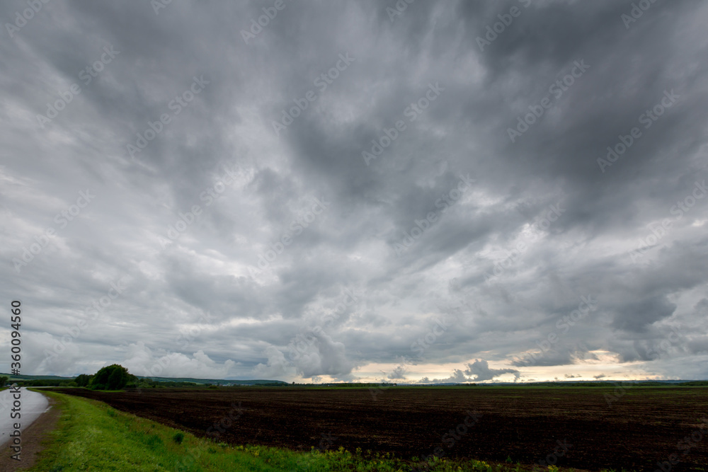 Obraz premium Stormy sky with fresh arable land and road in the corner