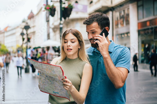 Couple of tourists holding a map and talking on a phone for an information