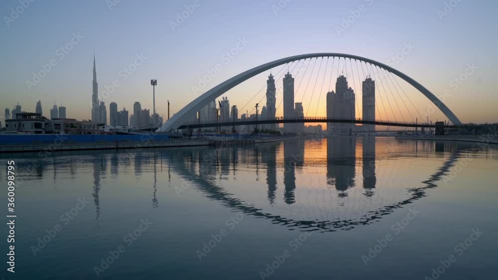 Dubai Canal - Dubai Water Canal Bridge Reflected In The Water With Downtown Skyline And Burj Khalifa On The Background At Sunset. - static shot Dubai Canal - Dubai Water Canal Bridge Reflected In The Water With Downtown Skyline And Burj Khalifa On The Background At Sunset. - static shot