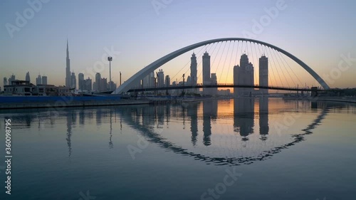 Dubai Canal - Dubai Water Canal Bridge Reflected In The Water With Downtown Skyline And Burj Khalifa On The Background  At Sunset.  - static shot photo