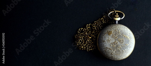 Dhaka, Bangladesh - April 25, 2020: A fashionable pocket watch with a golden chain in black background. Happy home photography during the quarantine. Stay home, stay safe.