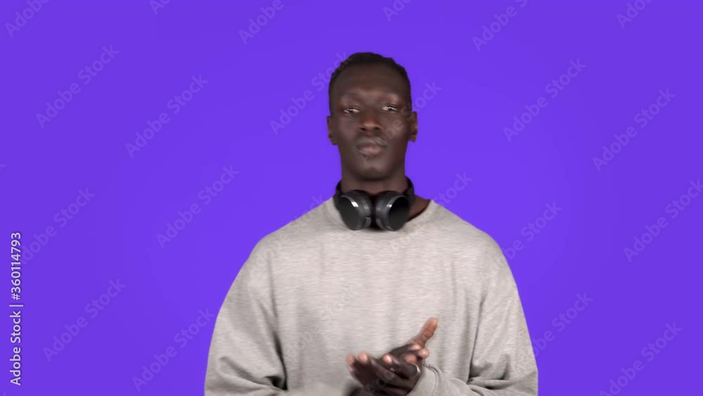 Clapping young african man, applauding in respect to someone. Isolated on blue background. Wearing white sweater and headphones on neck Clapping young african man, applauding in respect to someone. Isolated on blue background. Wearing white sweater and headphones on neck