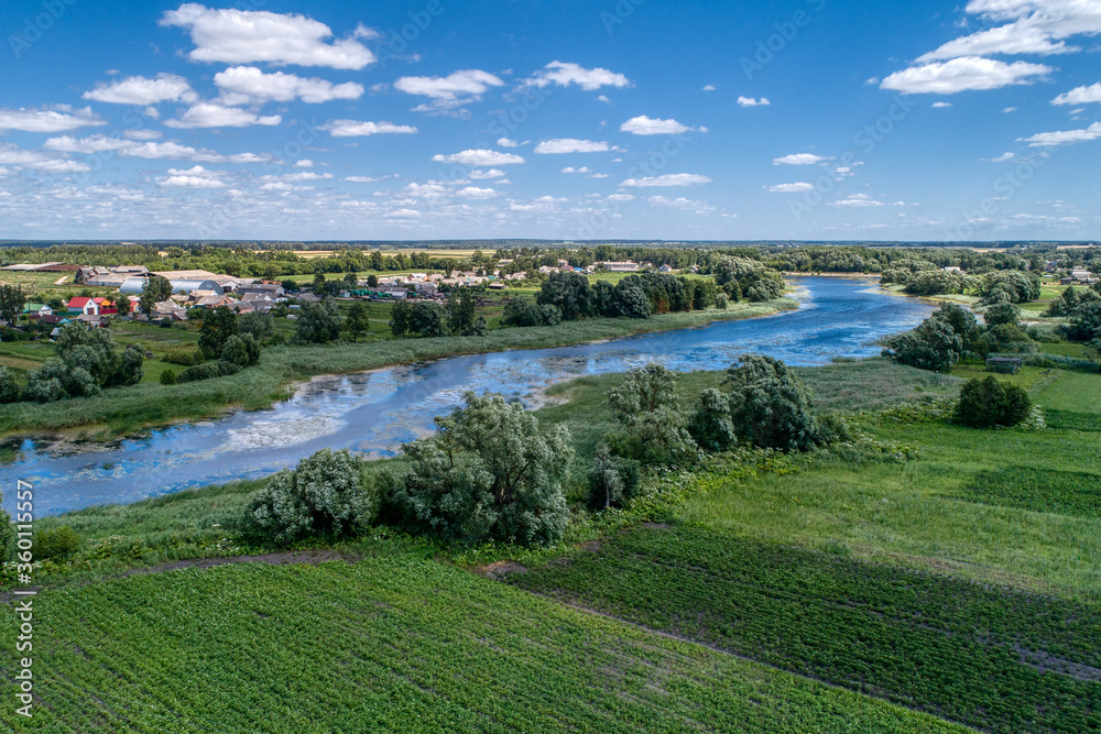 A small river flowing through meadows and agricultural fields. Aerial view. Evening shot with the setting sun.