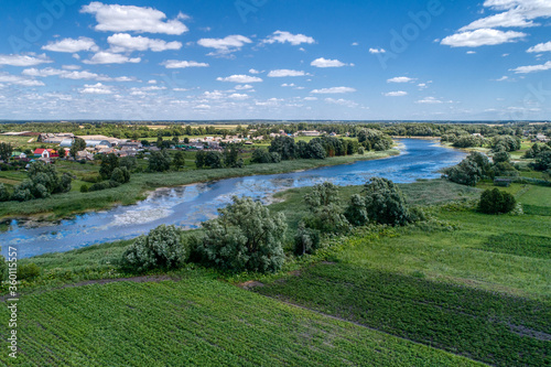 A small river flowing through meadows and agricultural fields. Aerial view. Evening shot with the setting sun.