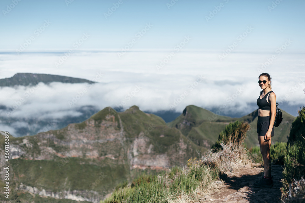 Small figure of sports girl on background of peaks and clouds. Mountain trekking, active tourism
