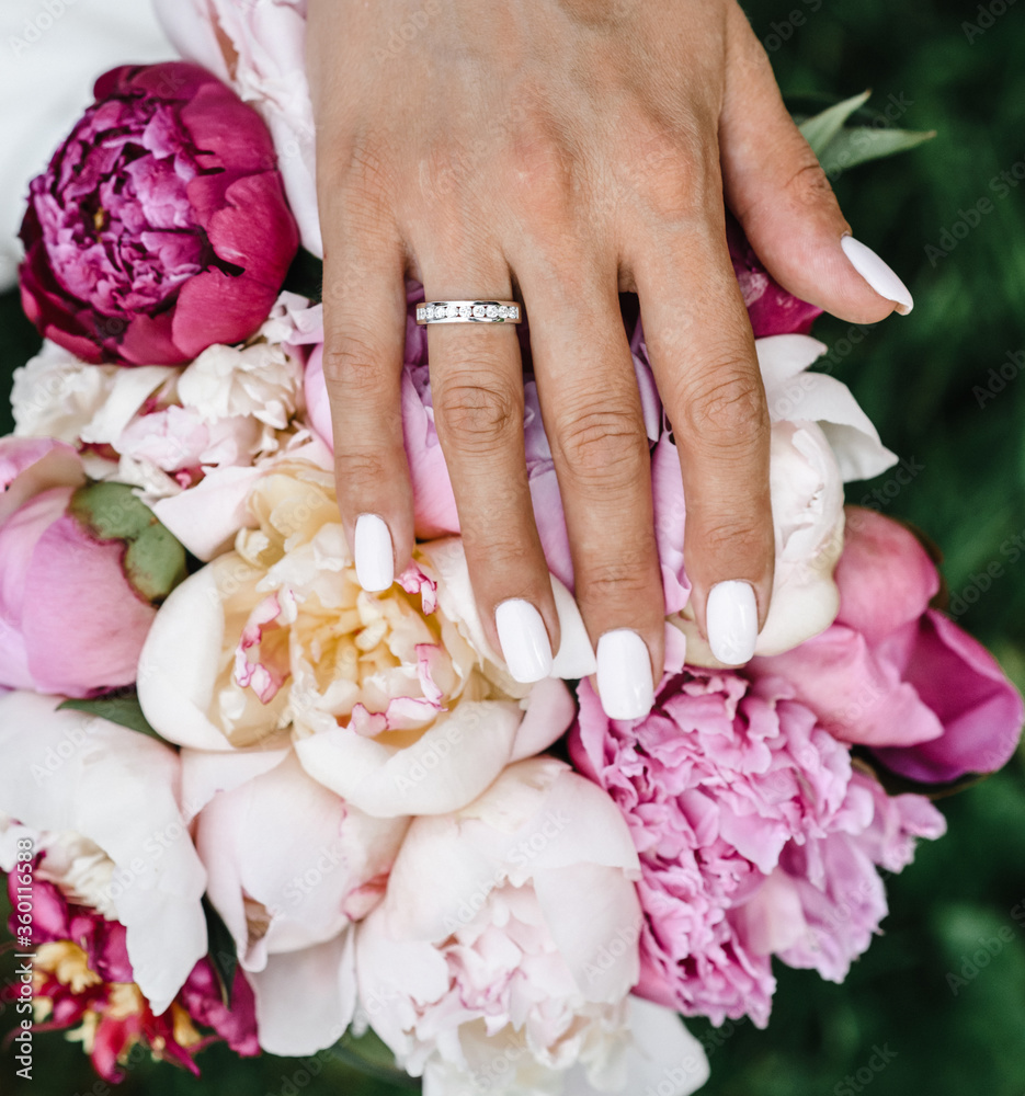 Fototapeta premium bride's hand with an elegant wedding ring with white gold diamonds on a bouquet of their peonies