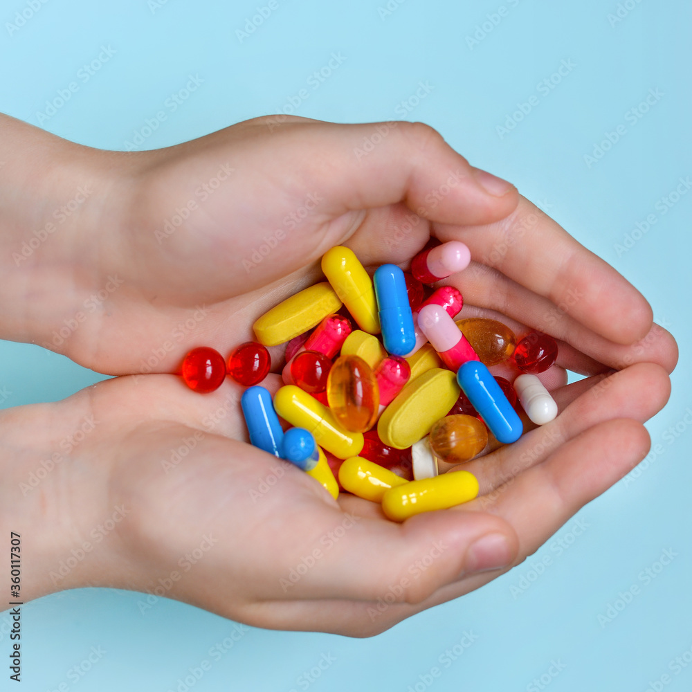 Child's hands hold many colorful vitamins, capsules, supplements, pills.