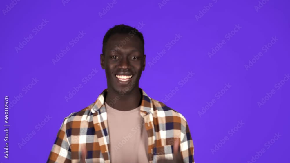 Happy, smiling african american man in good mood on blue background. Gesturing with thumbs up, like gesture, touching his plaid shirt - human emotions