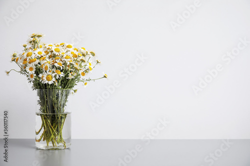 Vase with beautiful chamomiles on table against light background