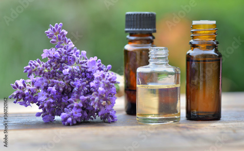 bottles of essential oil and bouquet of  lavender flowers arranged on a wooden table in garden