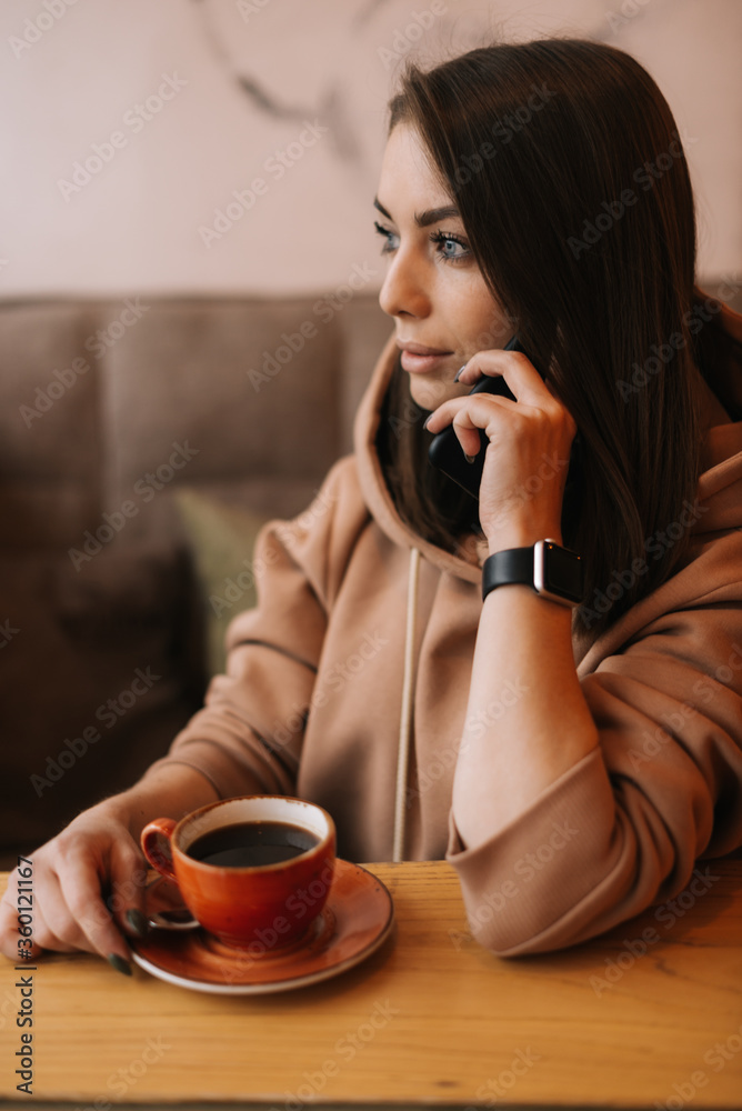 Portrait of handsome young woman in casual clothes talking on the phone at a table in a cozy cafe. Coffee cup on the table. Concept of leisure activity. Portrait of handsome young woman in casual clothes talking on the phone at a table in a cozy cafe. Coffee cup on the table. Concept of leisure activity.