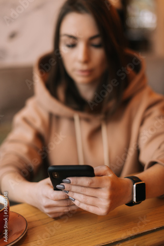 Serious focused young woman reading text message on mobile phone at restaurant. Pretty girl in casual clothes typing on the phone at cafe. Cup of coffee on the table. Concept of leisure activity.