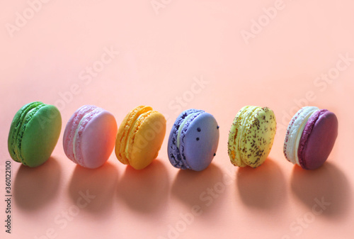 Colorful macaroon desserts in a row on the orange colored background