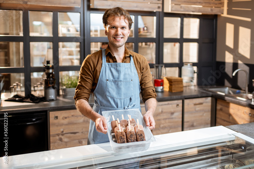 Portrait of a handsome seller working with ice cream at the counter of pastry shop or cafe