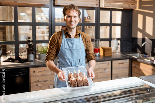 Cuadro en lienzo Portrait of a handsome seller working with ice cream at the counter of pastry sh
