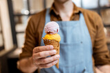 Seller in apron holding ice cream in a waffle cone, close-up. Selling ice cream in a shop
