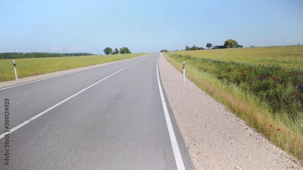 Winding asphalt road in Latvia. Along the edges sown fields of argo with cereals to the horizon. Red poppies on the sidelines. Baltic state Winding asphalt road in Latvia. Along the edges sown fields of argo with cereals to the horizon. Red poppies on the sidelines. Baltic state