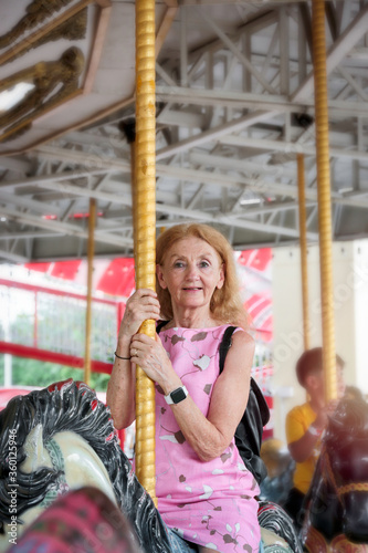 Elderly spending time at theme park on weekend  senior woman hanging out and having fun at amusement park. Grandma enjoying riding on a merry go round at carousel spinning