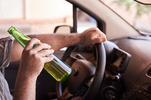 An unrecognizable man drinking beer while driving car. Concepts of driving under the influence, drunk driving or impaired driving photo