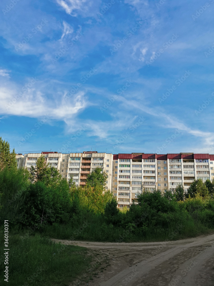 view from the forest to a modern residential building under a blue summer sky