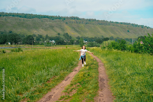 A child a girl runs happily with her arms outstretched in rural summer nature against the backdrop of mountains and a lake