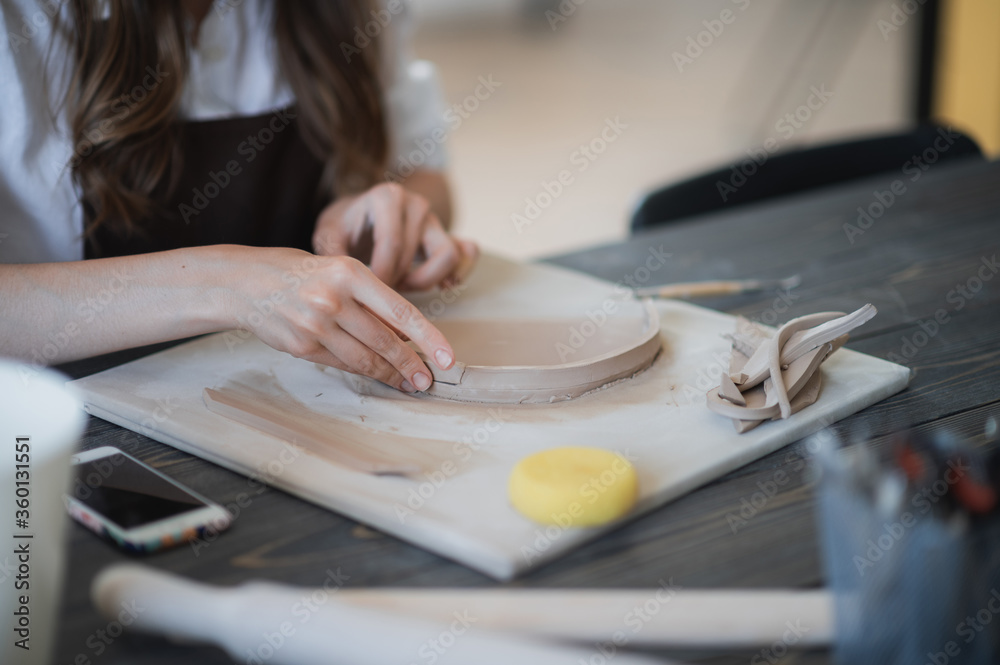 Woman's fingers adding and adjusting a clay part on a future ceramic product.