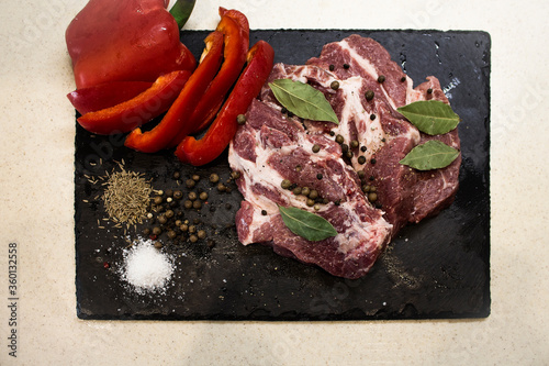 Juicy raw meat with vegetables and seasonings on a black background. Composition of meat. The process of preparing a meat dish.