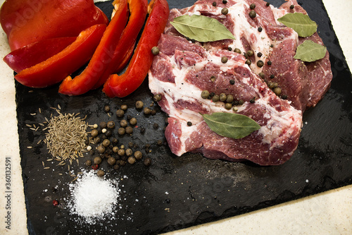 Juicy raw meat with vegetables and seasonings on a black background. Composition of meat. The process of preparing a meat dish.