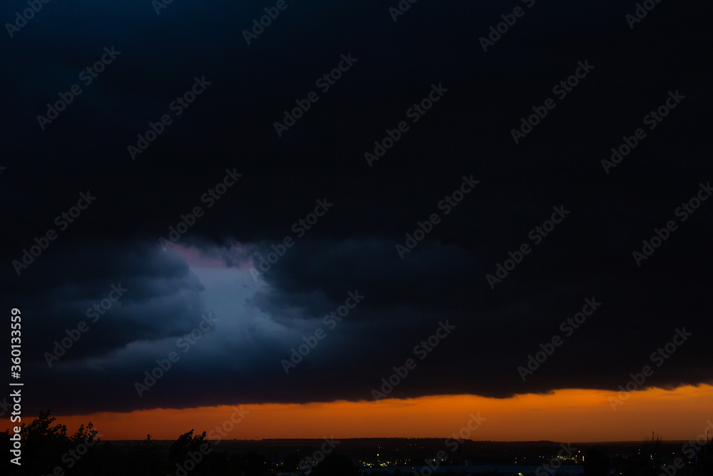 Fototapeta premium Black thunderclouds at sunset. Bright orange sunset and dark clouds. Storm sky