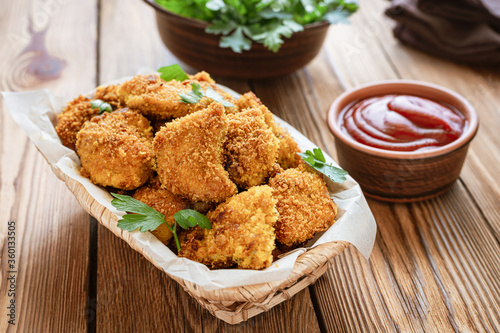 Homemade chicken nuggets in basket on wooden background