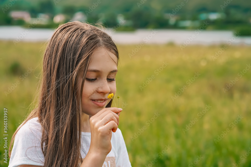 A little girl child gently holds a flower in her hands in the countryside against the background of mountains and f A little girl child gently holds a flower in her hands in the countryside against the background of mountains and f