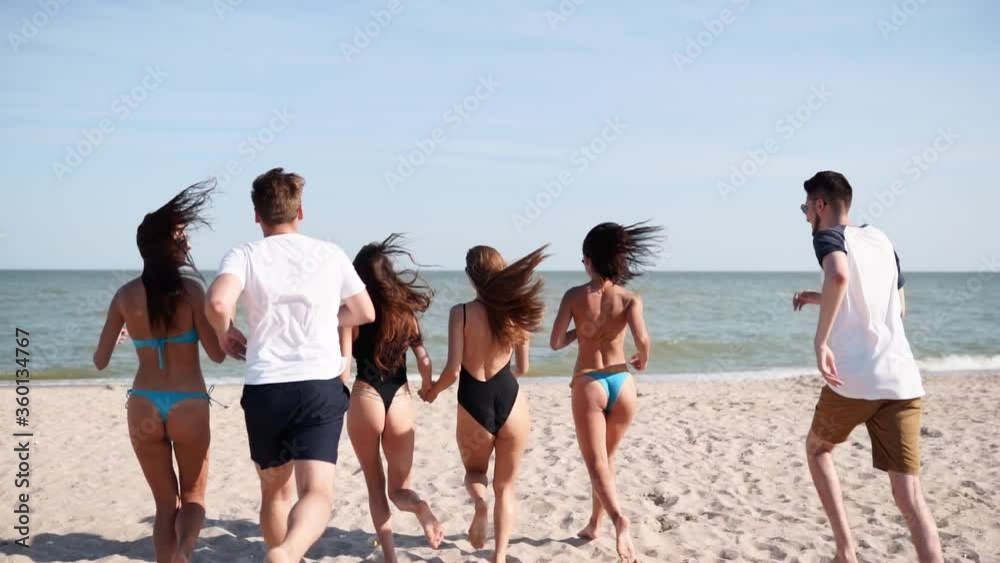 Group of happy friends running to sea water and jumping on sandy beach. Cheerful people having fun on the seaside on summer sunny day. Young men and women go to swim into ocean. 120 fps slow motion. Group of happy friends running to sea water and jumping on sandy beach. Cheerful people having fun on the seaside on summer sunny day. Young men and women go to swim into ocean. 120 fps slow motion.