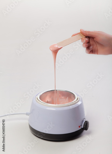 Wax melter on a white background. Salon equipment. Wooden spatula in female hands.