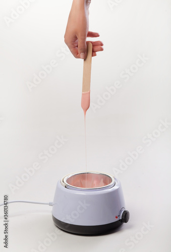 Wax melter on a white background. Salon equipment. Wooden spatula in female hands.