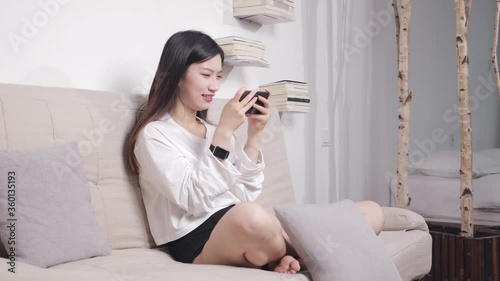 The beautiful woman sitting on the sofa uses her mobile phone to play games. photo