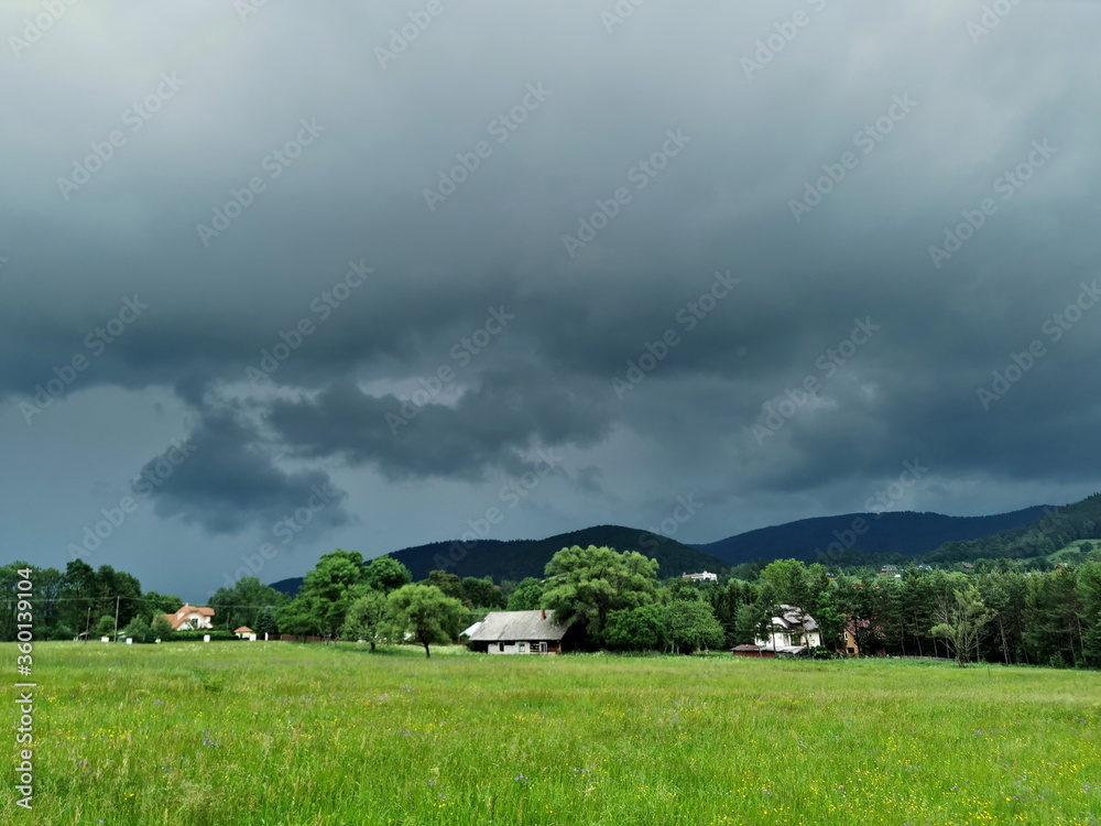 Obraz premium Poland Low Beskids Wysowa Zdroj. Storm clouds on the village. Green meadow with flowers.