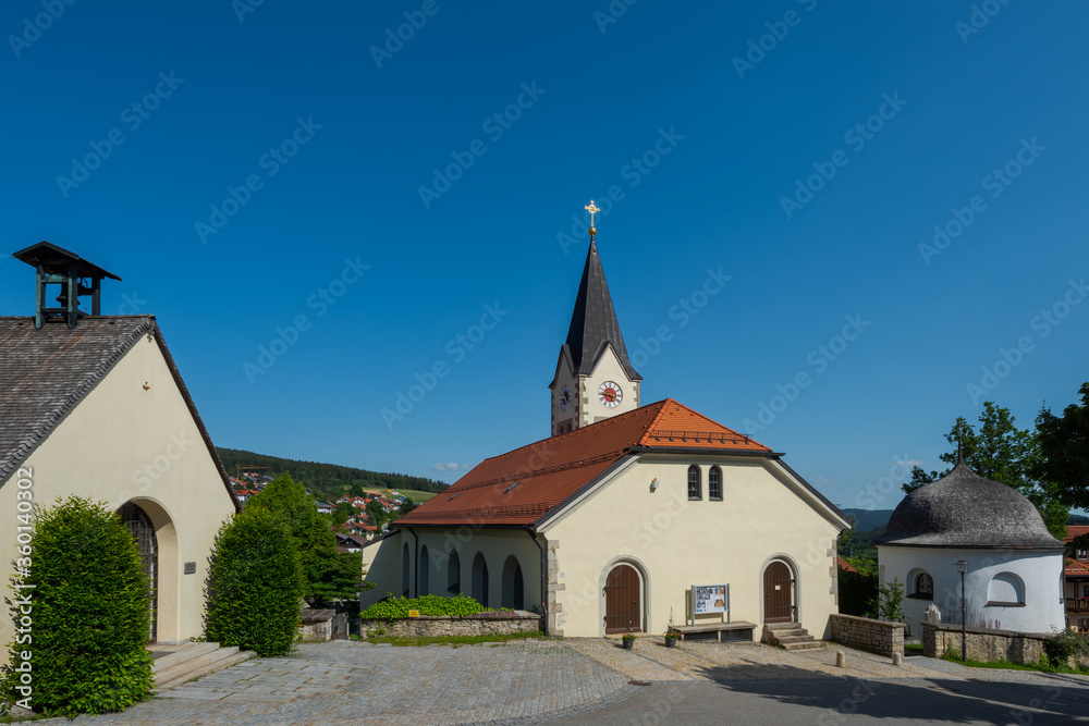 Pfarrkirche und Kirchplatz im Ortskern von Sankt Englmar im Bayerischen Wald in der Oberpfalz in Bayern im Sommer bei blauem Himmel