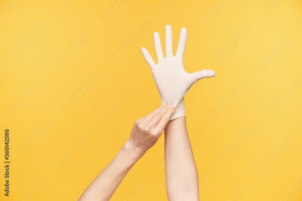 Indoor photo of young female's hand being raised while taking on rubber glove and keeping all fingers separately, isolated against orange background